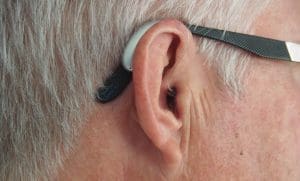 Close up of an older man wearing glasses and an electronic hearing aid.