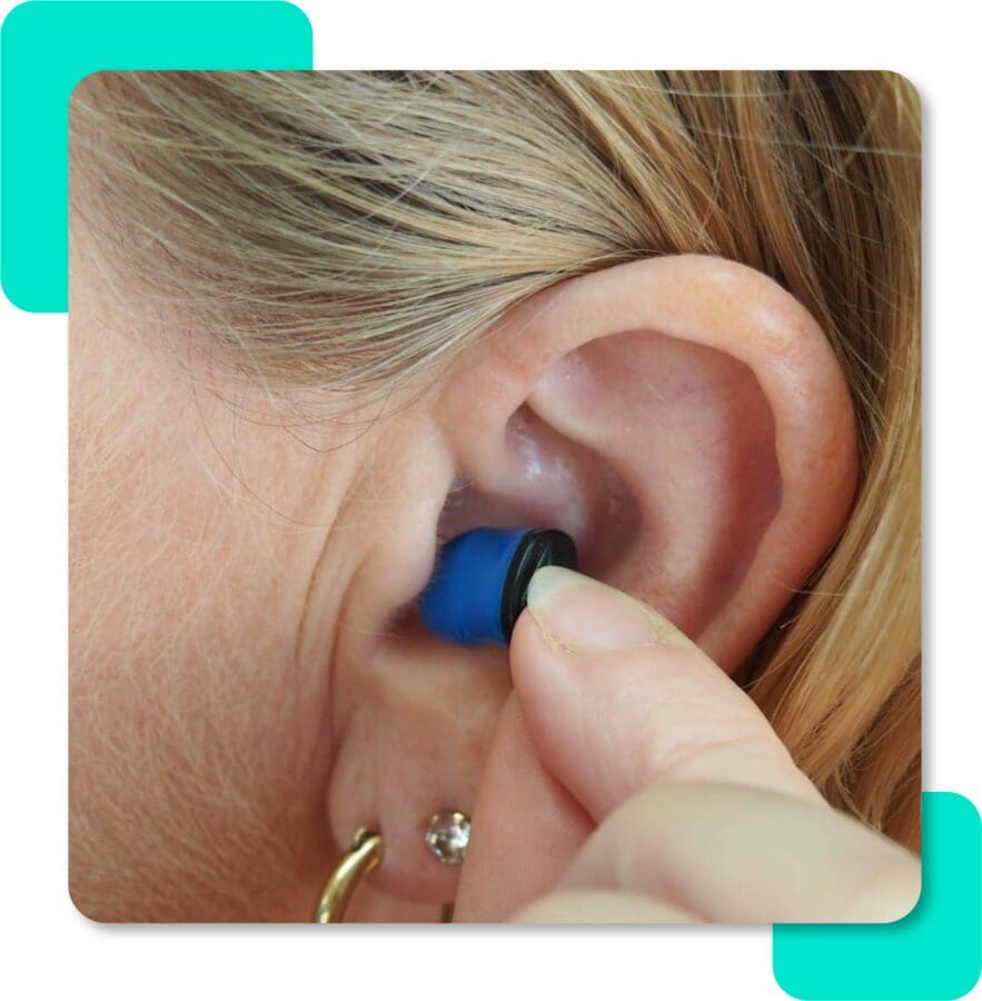 A woman inserts a small hearing instrument into her ear canal