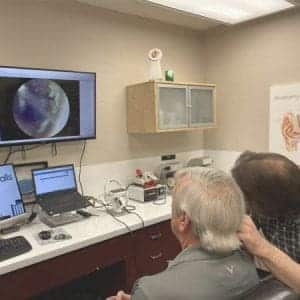 A man has his ear examined with a video otoscope and his ear canal is displayed on a screen as a part of hearing aid service and repair